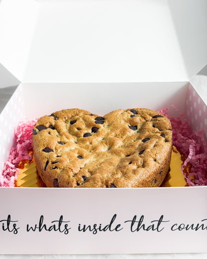 Heart-shaped chocolate chip cookie in a box with pink tissue paper.